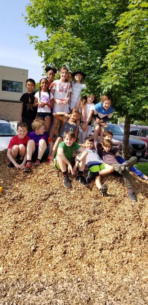 Students sit together on a huge pile of wood chips.
